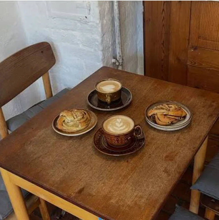 To kopper kaffe med latte art og to hjemmebagte snegle på et lille træbord hos Lagoni & Co.